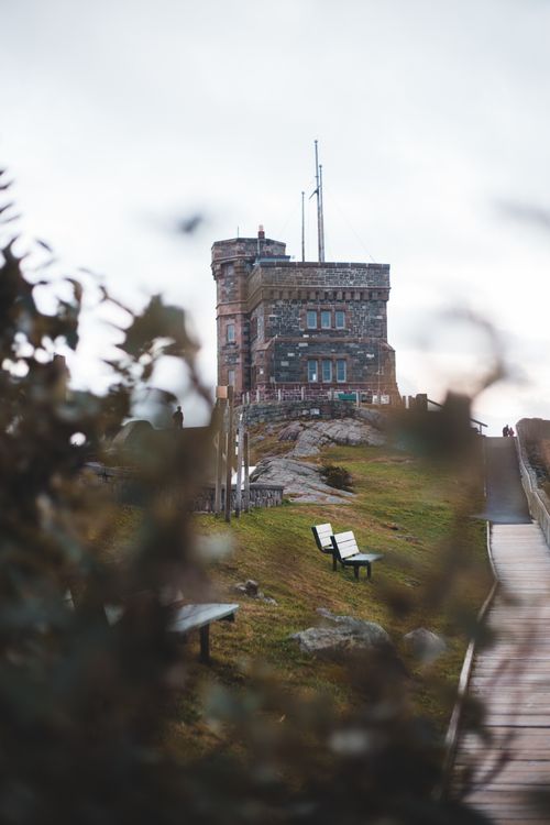 Free A stone tower stands on a hilltop beside benches and a boardwalk pathway, surrounded by foliage. Stock Photo
