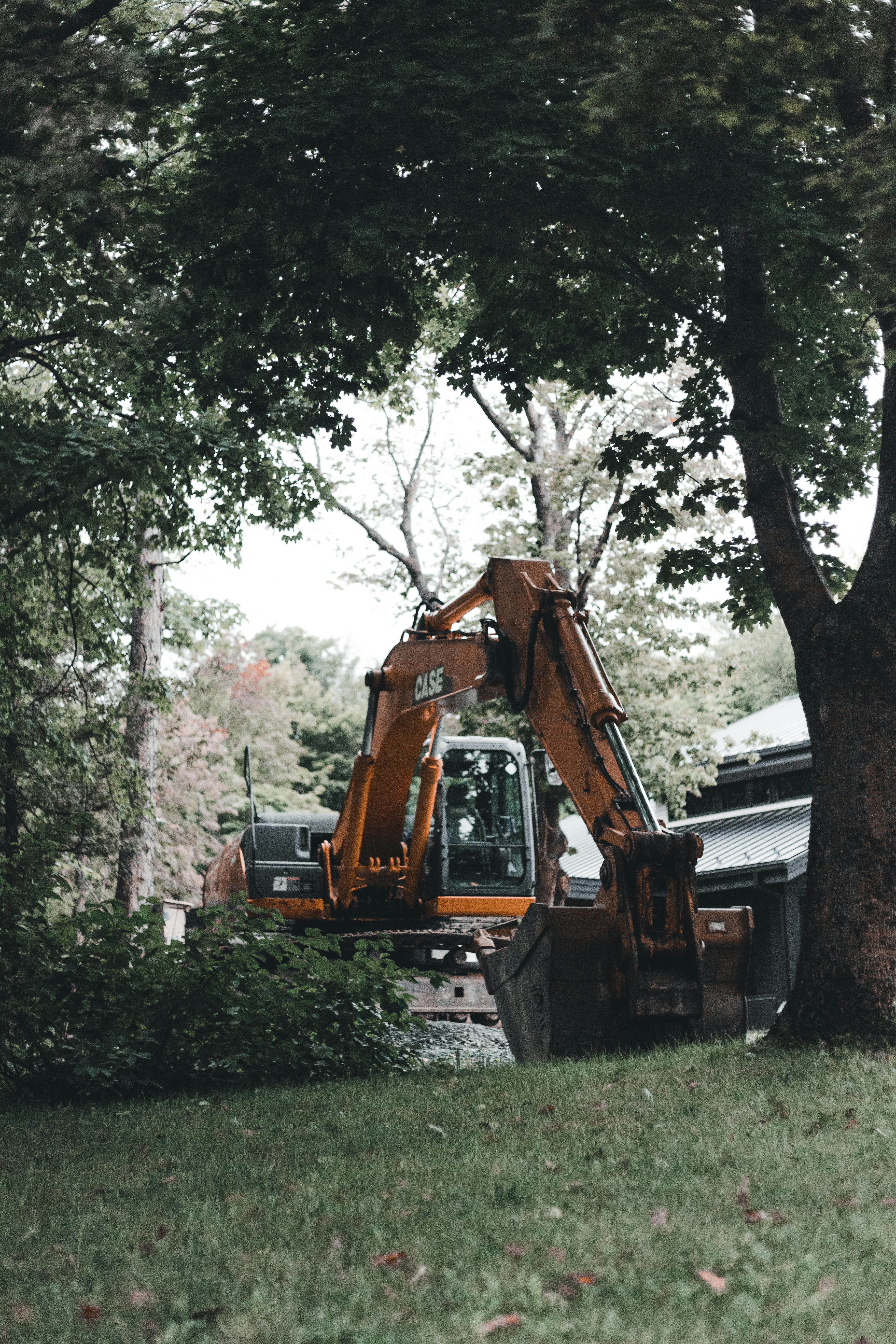 Excavator working in a lush green suburban yard with mature trees