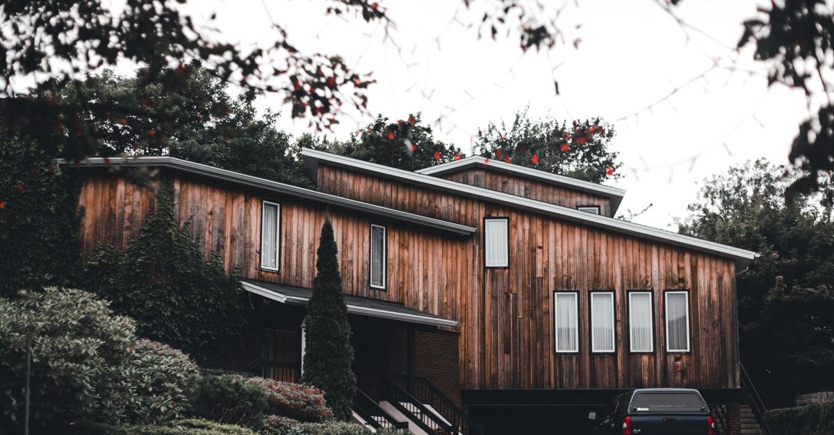 Stylish modern wooden home exterior with greenery and a parked black car.