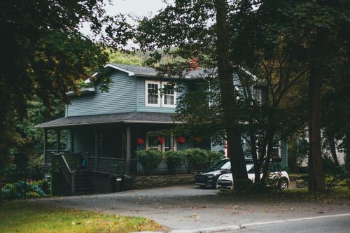 Free A cozy two-story suburban house nestled among lush trees, conveying serenity and seclusion. Stock Photo