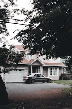 A modern suburban house with a parked car on the driveway surrounded by trees.