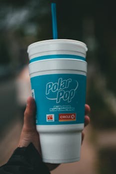 Hand holding a Polar Pop cup with a straw, outdoor shot in a blurred background
