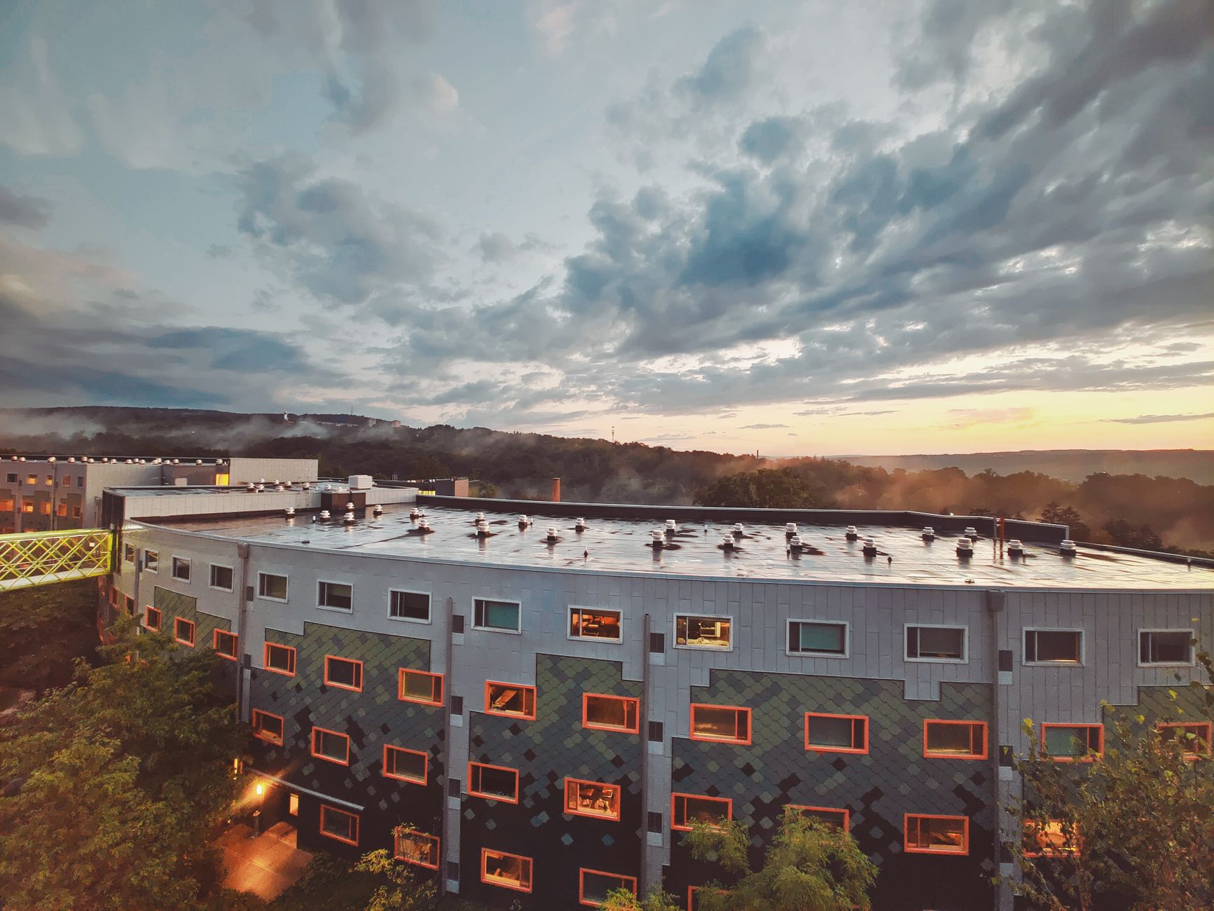 Aerial view of a modern building with unique architecture surrounded by greenery during a vibrant sunset in Ithaca, NY.