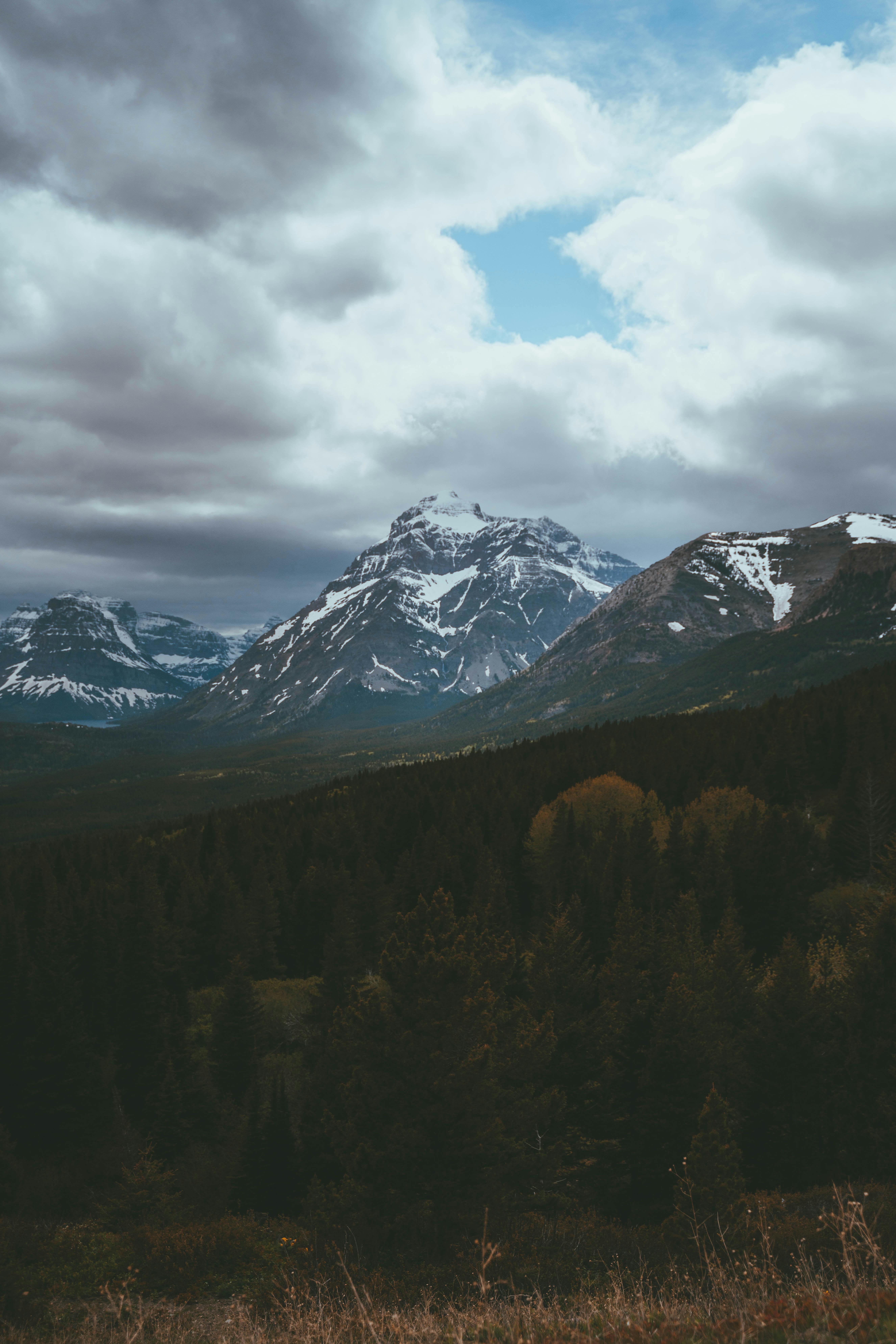 Majestic snow-covered mountains rise under a dramatic cloudy sky, offering a breathtaking natural landscape.