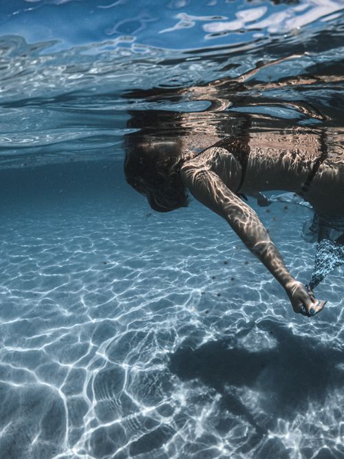 Free Underwater view of a woman swimming in a sunny pool with clear blue water. Stock Photo