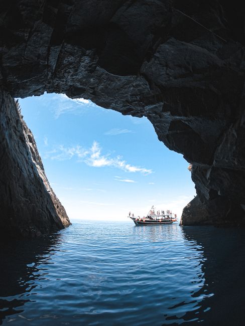 A peaceful view of a boat sailing through the entrance of a rocky ocean cave under a clear blue sky.
