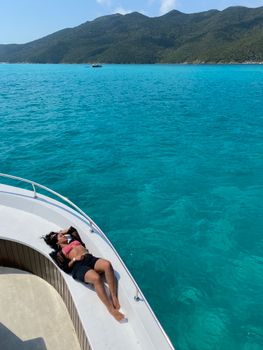 Woman sunbathing on a yacht, surrounded by stunning turquoise sea against scenic mountains.