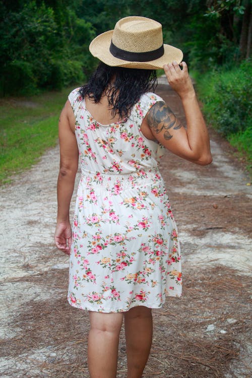 Young Woman Wearing a Floral Dress and a Sun Hat Walking Outdoors