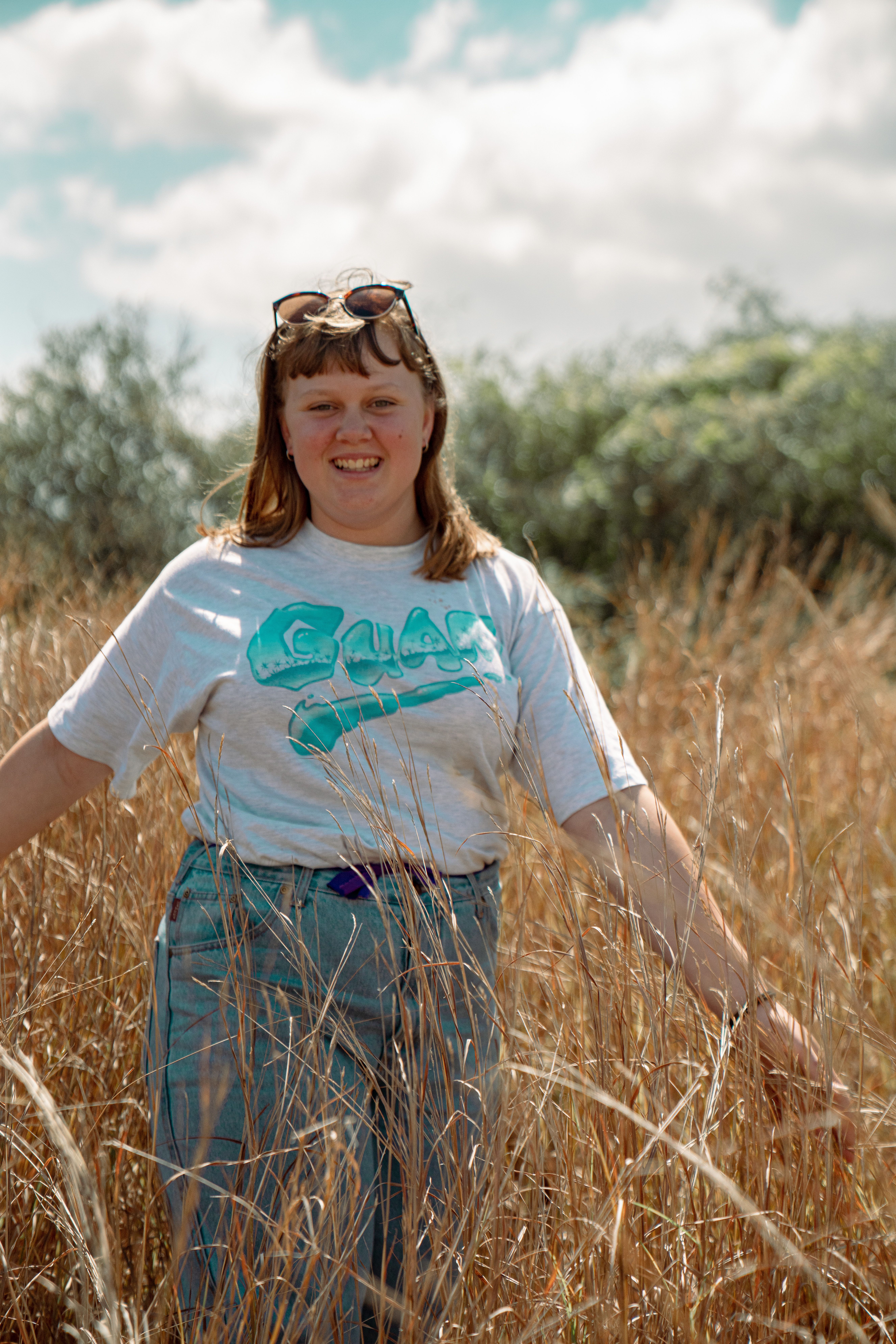 Smiling woman standing in sunlit field of dried grass. Bright and carefree outdoor scene.