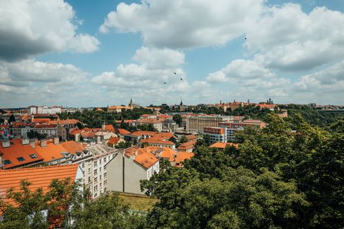 Free A beautiful panoramic view of a historic city with orange rooftops and lush greenery under a cloudy sky. Stock Photo
