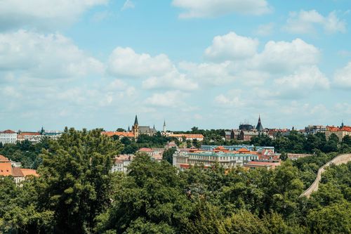 Free A panoramic view of Prague's historic cityscape with lush greenery and a clear blue sky. Stock Photo
