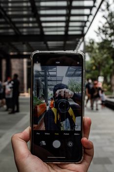 A smartphone held up capturing an urban scene in HDR mode, reflecting the photographer.