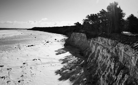 Black and white photo of a dramatic coastal cliff with sunlight casting shadows.