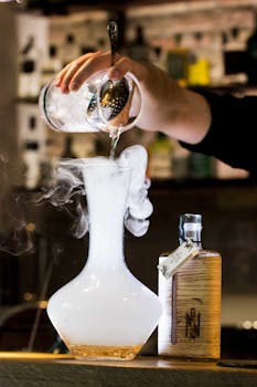 Bartender pouring a cocktail into a misty glass decanter creating a dramatic effect.