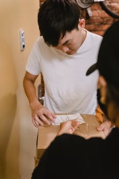 Young man in casual clothing receiving a delivery package indoors, focusing on package details.