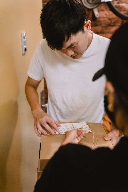 Free Young man in casual clothing receiving a delivery package indoors, focusing on package details. Stock Photo