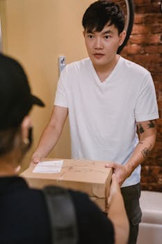 An Asian man in casual clothing receives a delivery package indoors, exuding a professional yet casual vibe.