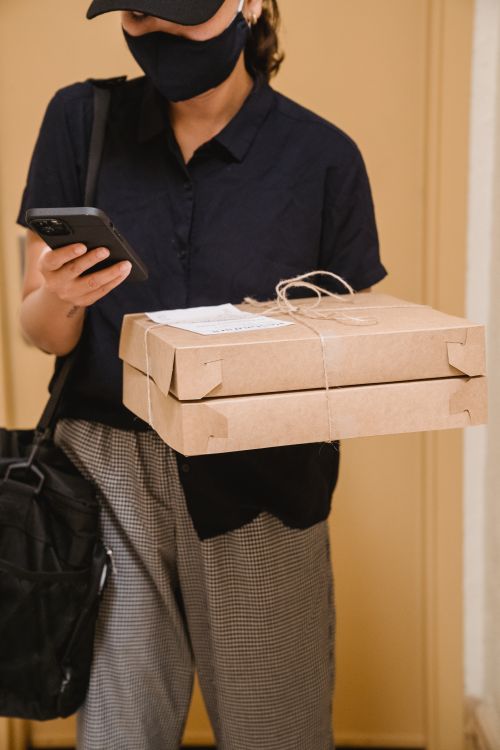 Free Woman in a face mask holding packages and a smartphone, representing delivery service. Stock Photo