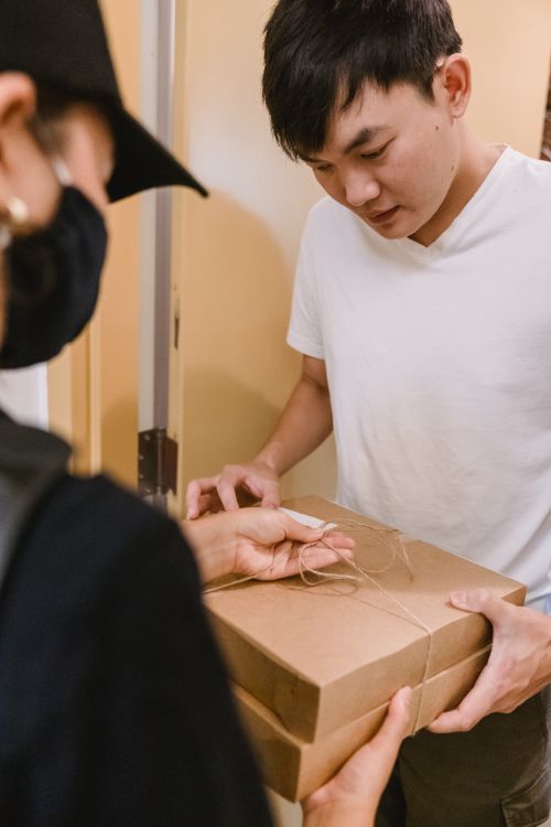 Free A man receives a delivery package from a courier wearing a mask indoors. Stock Photo