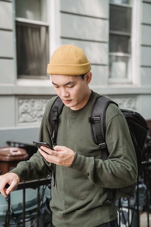 Man in Green Jacket and Orange Knit Cap Using Smartphone