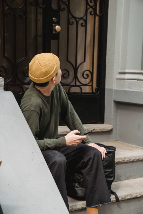 Free A delivery person sitting on stairs with phone, looking away outdoors. Stock Photo