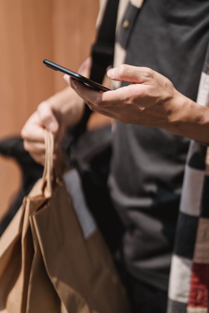 Shopper holding a phone while carrying paper bags in a store — photo by Mike Jones on Pexels