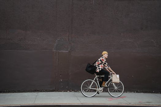 A courier riding a bicycle with bags along a city street against a concrete wall.