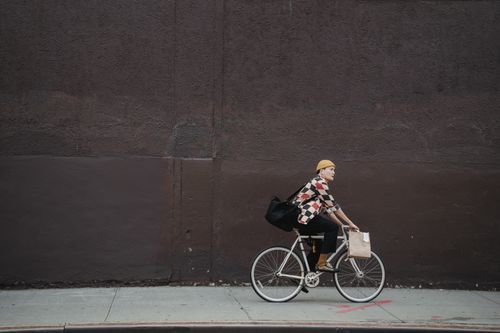 Free A courier riding a bicycle with bags along a city street against a concrete wall. Stock Photo