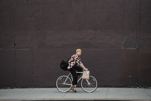 A delivery person riding a bicycle on an urban street against a large dark wall.