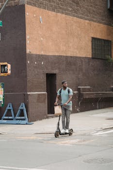 A man riding an electric scooter with a shopping bag in an urban outdoor setting.