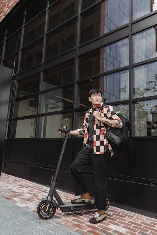 A Man in a Checkered Shirt Standing on His Scooter
