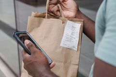 Man holding a paper shopping bag with a receipt, using a smartphone outdoors.