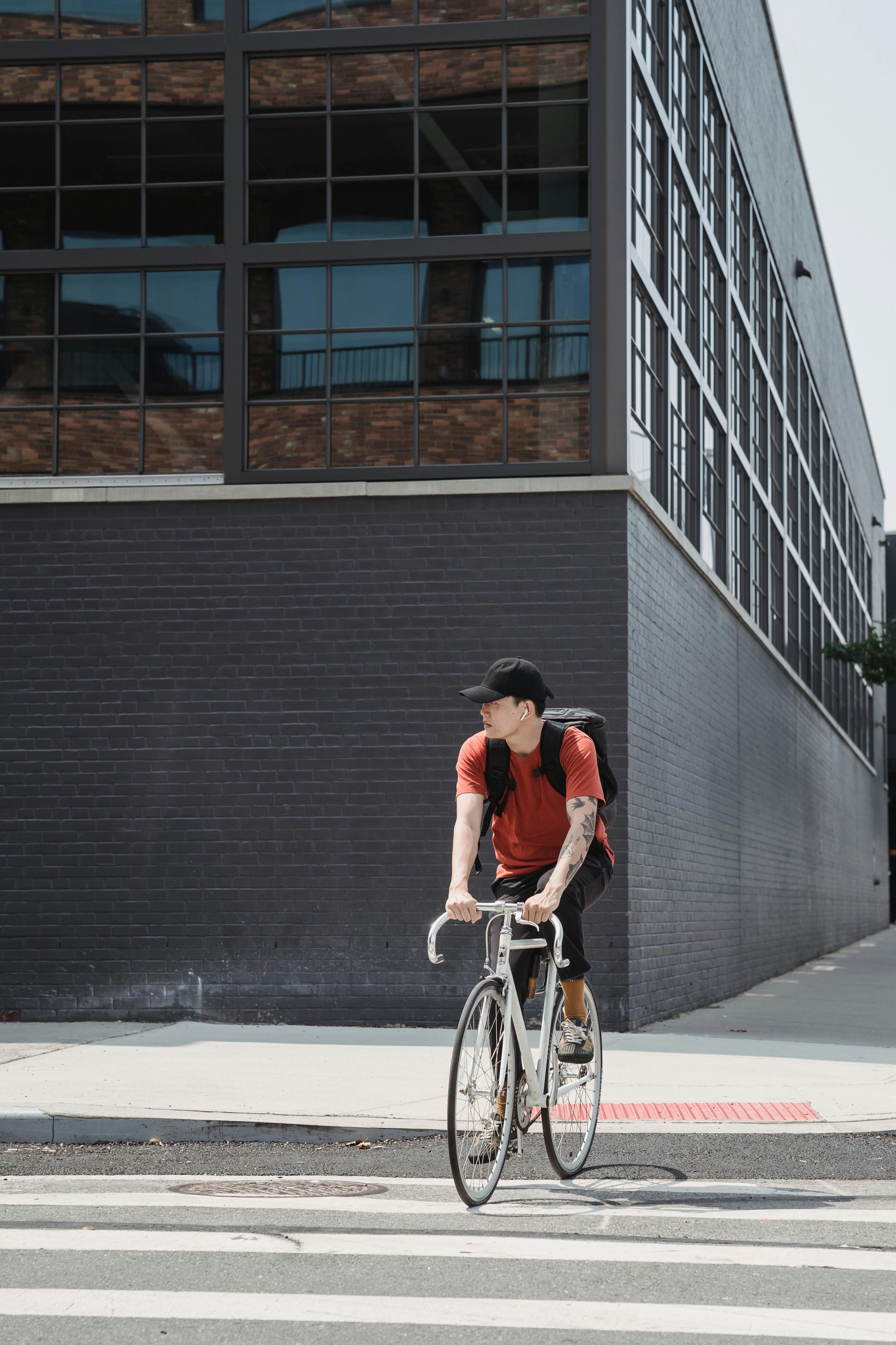 Free Man cycling on a city street with a backpack, showcasing modern urban lifestyle and transport. Stock Photo