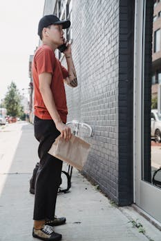 Man delivering food in the city while talking on the phone, holding a paper bag.