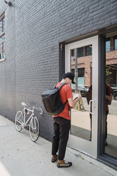 Bicycle courier delivering a package in an urban setting with a reflective glass door.