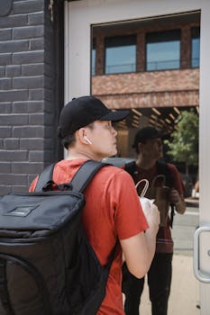 Young male food delivery worker at doorstep, carrying a backpack and food bag.