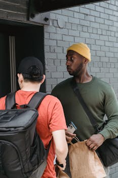 Two delivery couriers interact outside a building entrance, exchanging packages as they work efficiently.