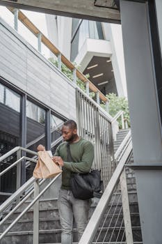 Man carrying a fast food order in an urban setting, walking down stairs.