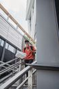 Man in Red Jacket and Yellow Cap Standing on Gray Staircase