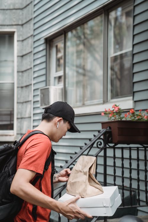 Free A young male delivery man carrying a pizza box and a paper bag, walking up residential steps. Stock Photo