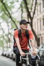 Man in Orange and Black Shirt and Black Pants Wearing Black Cap Sitting on Black Metal