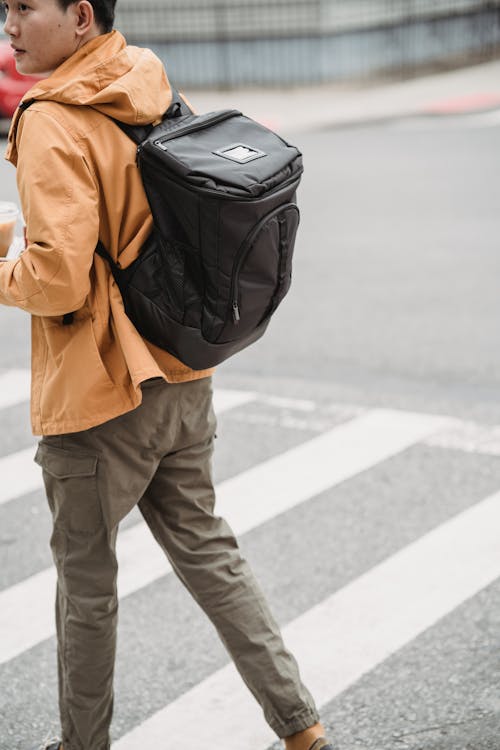 Photo of a Man with a Black Backpack Walking on a Pedestrian Lane