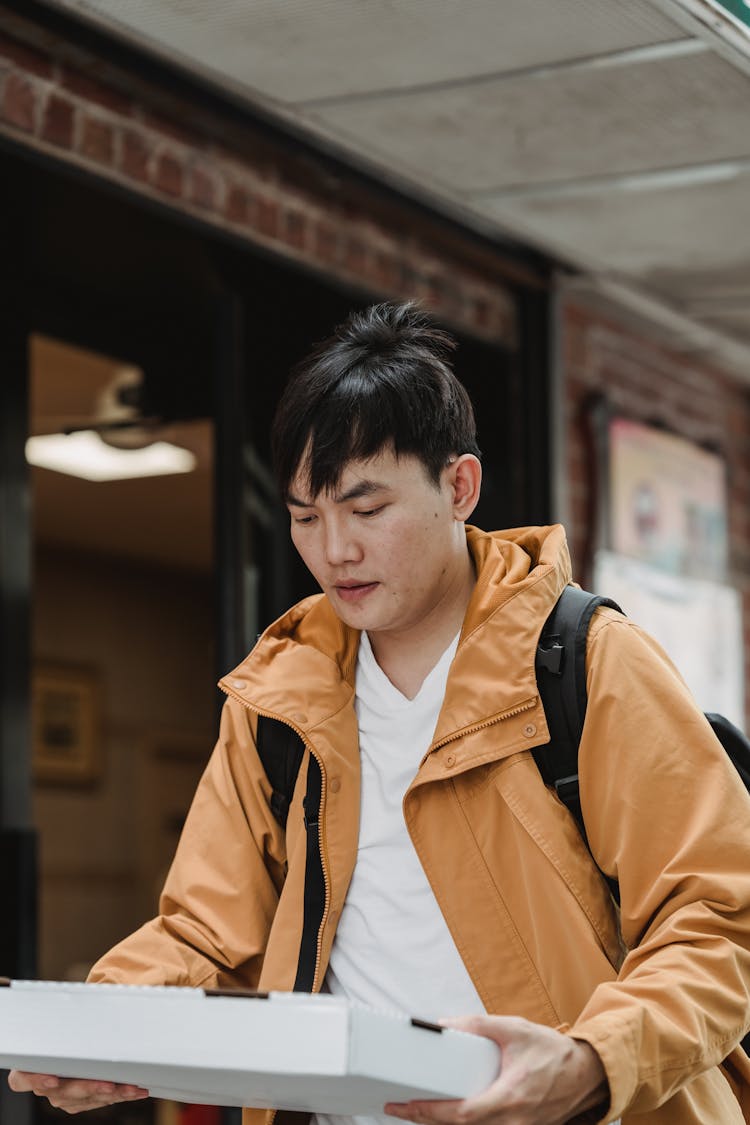 A Man In Brown Jacket Holding White Box