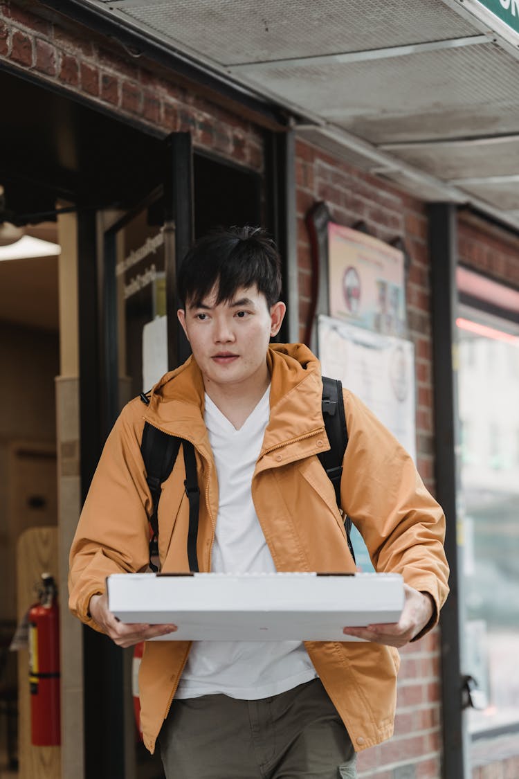 Photo Of A Man In A Jacket Holding A Box Of Pizza