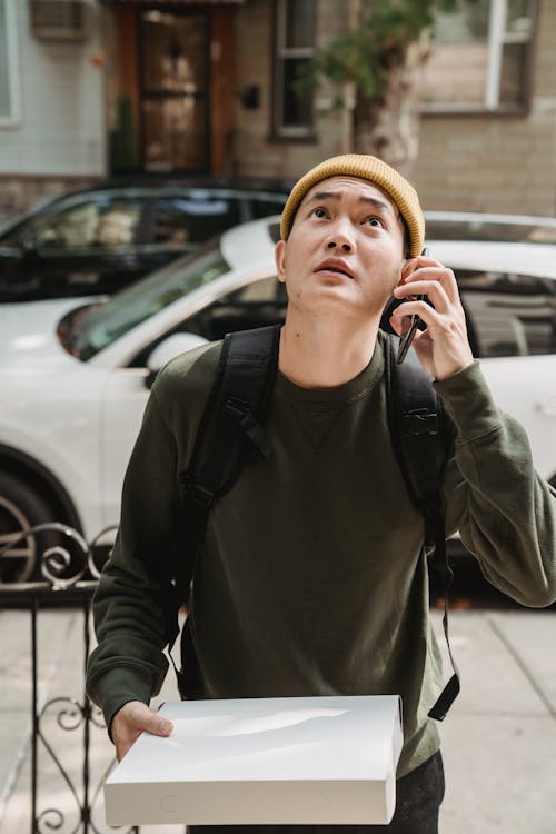 Man Holding a Pizza Box Using a Cellphone