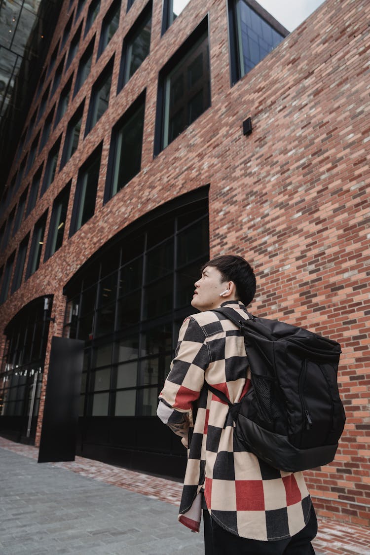 Man With Backpack Walking Near Brick Building