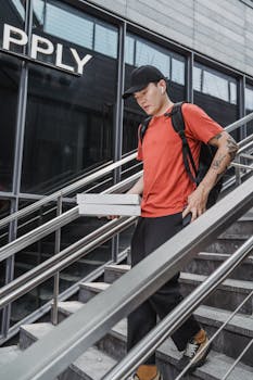 A young man in casual wear delivers pizza on city steps, embodying modern urban lifestyle.