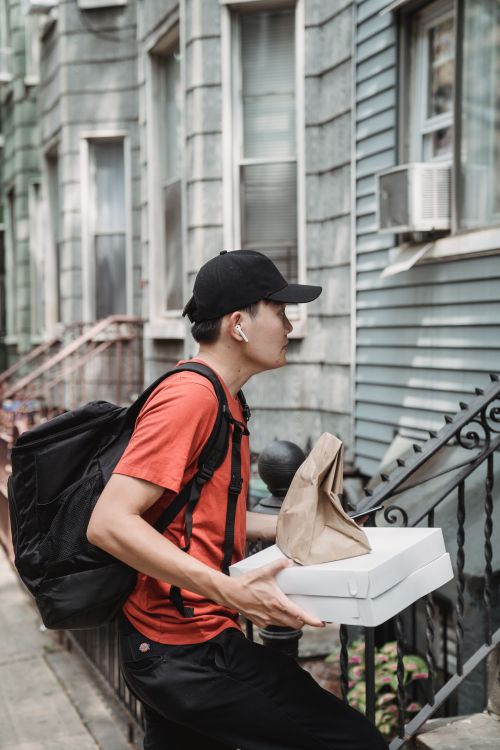 Free A young delivery man carries pizza boxes to an urban doorstep, showcasing modern food delivery service. Stock Photo