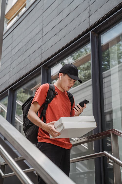 A Delivery Person Checking his Phone While Holding Packages