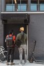 Man in Green Jacket and Brown Pants With Black Backpack Standing Beside Black and Gray Bicycle